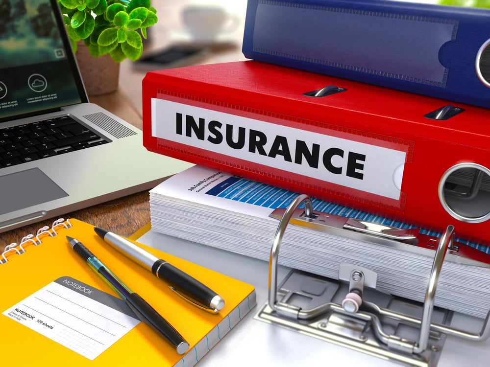 Red Ring Binder with Inscription Insurance on Background of Working Table with Office Supplies, Laptop, Reports. Toned Illustration. Business Concept on Blurred Background.-1