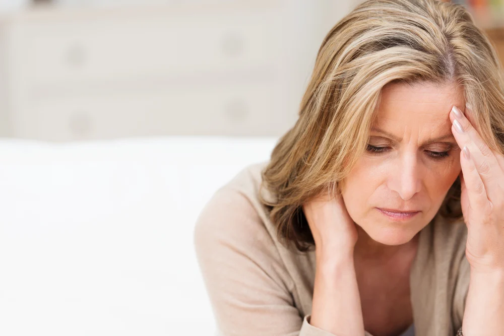 Woman suffering from stress or a headache grimacing in pain as she holds the back of her neck with her other hand to her temple, with copyspace